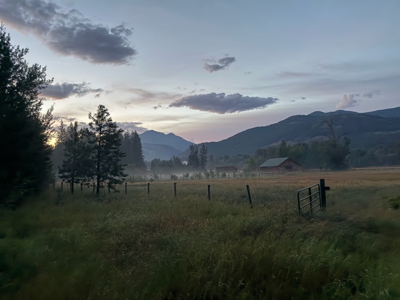 Dawn mist over the farm pasture with a gate and mountains beyond